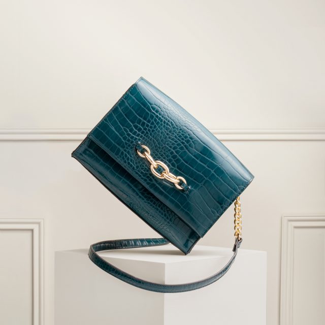 A shot from a creative still life shoot; Amelia was shoot assistant. This shot shows a cross-body handbag balanced on its corner, with a panelled wall in the background.